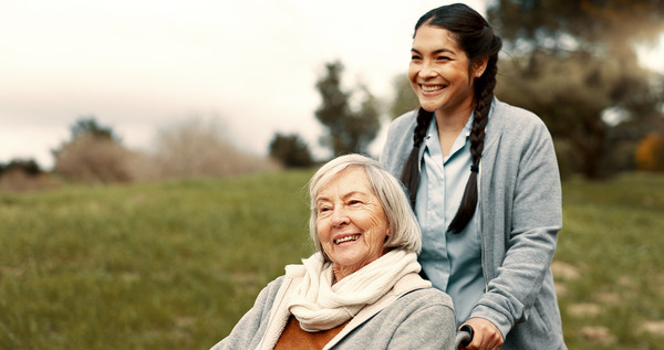 A nurse pushing a woman in a wheelchair outdoors 