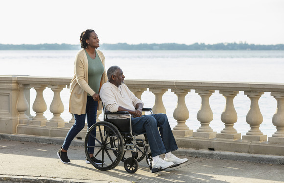A woman pushes an older man in a wheelchair outside 