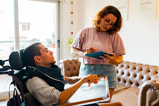 A man in a wheelchair communicating with his sister who is holding a tablet 