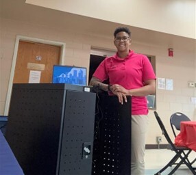 A picture of a person standing in front of a laptop which is rested on a table