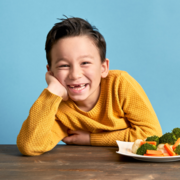 Young boy with toothless grin smiling about a plate of veggies