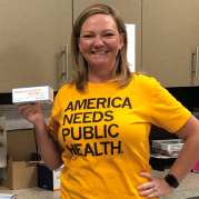 Amy wears a America Needs Public Health shirt and holds vaccine
