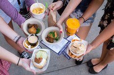 Several hands hold out different food items at Taste of Iowa City