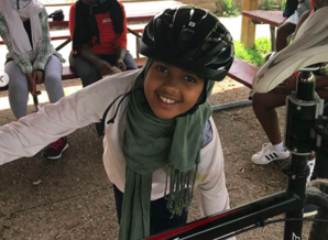 A young girl smiles, wearing a helmet standing next to a bike