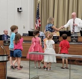 Mayor Throgmorton shakes Tricia Windschitl's hand with several preschoolers at city council meeting