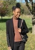 Black girl standing in pink sweater and black jacket smiling at the camera