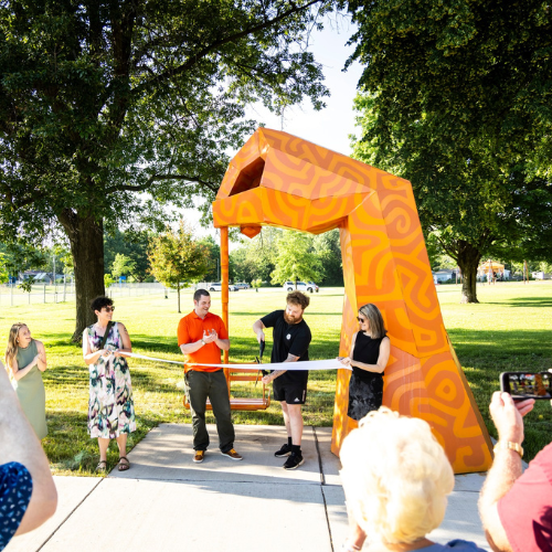 Attendees celebrate during a ribbon-cutting ceremony in Iowa City of the large orange "Uplift" sculpture .