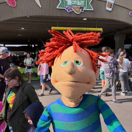 A puppet in a green and blue shirt promotes the Farmers Market in a sign-along