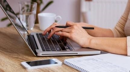 Woman working on keyboard with phone and notebook nearby on table