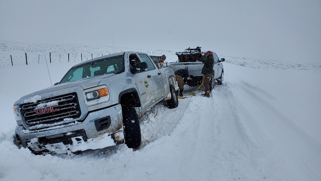 Truck in snow pulling another truck out of a ditch