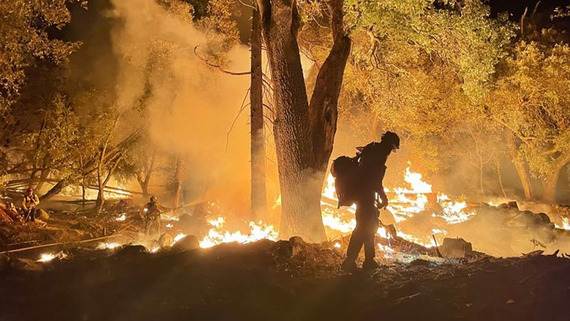 Wildfire at night silhouettes a lone firefighter