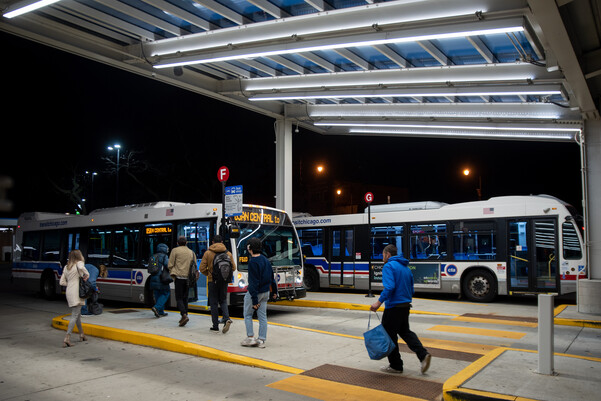 People walking to buses parked at a bus terminal at night