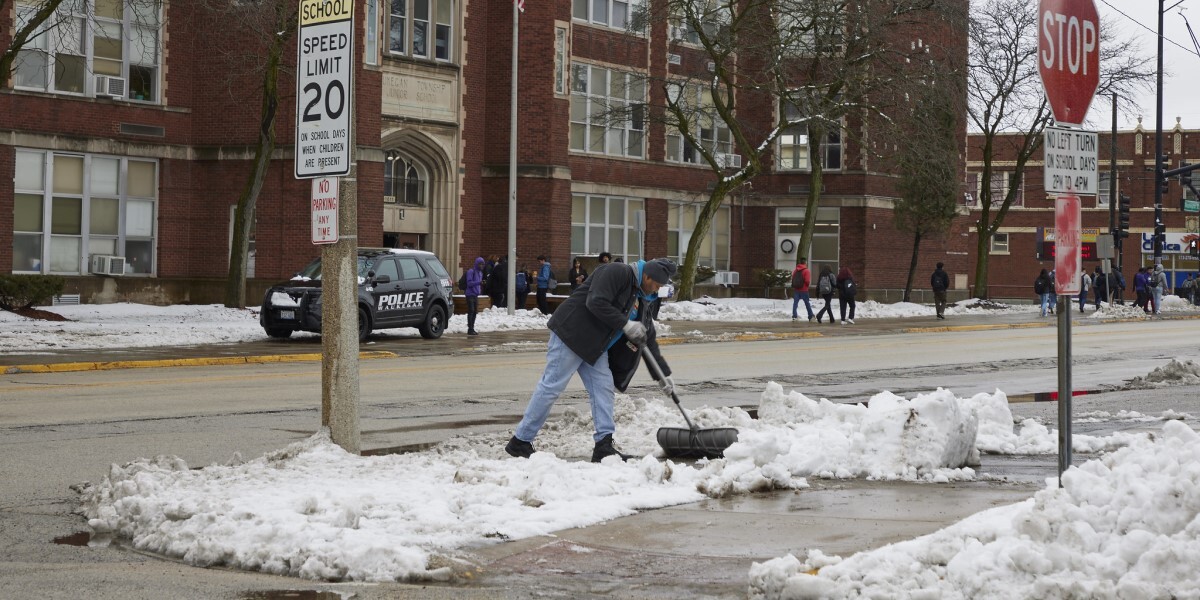 Person shovels sidewalk across the street from school