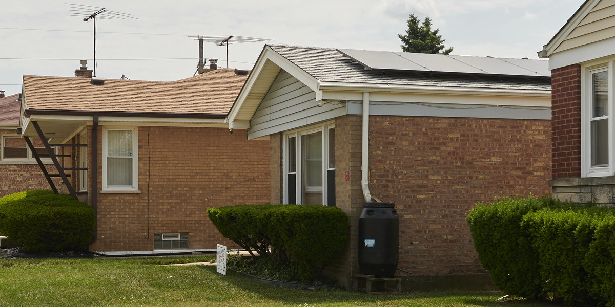 House with solar panels on roof and rain barrel connected to downspout
