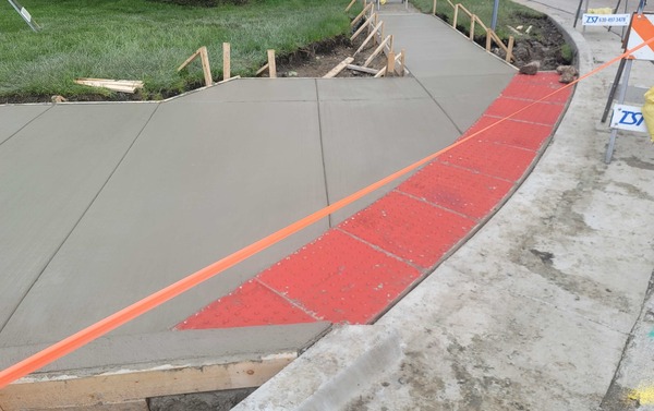 Photograph of sidewalk construction: newly poured concrete sidewalk with bumpy warning tiles for visually impaired people