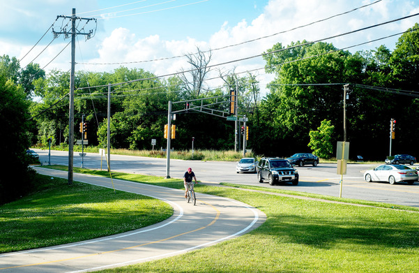 Photograph of a man riding his bike on a curving bike trail near a road