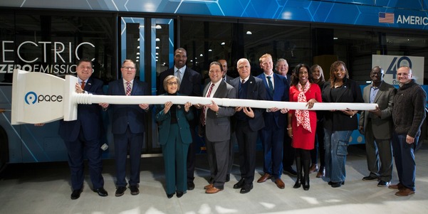 Elected officials and Pace leaders posing in front of electric bus with oversized electical plug