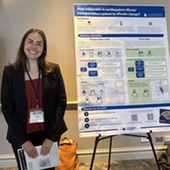 Woman smiles while standing next to poster