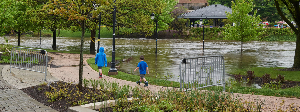 Two kids walk along flooded riverwalk. Lamp posts stick out of the water due to flooding