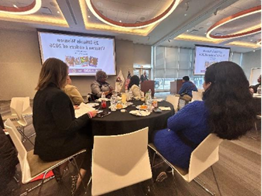 Two women sitting at a table looking at a presenter and PowerPoint presentation.