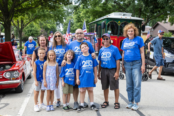  Mayor, city manager, elected officials, and others stand in the street at the Des Plaines Independence Day Parade wearing matching blue shirts