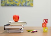 Apple on stack of books, next to coloring pencils and alphabet blocks