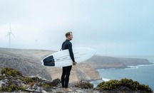 Photograph of surfer Josh Kerr holding a surfboard made from a wind turbine