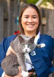 Rachel in graduation gown holding Alvin a gray and white cat