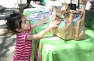 young girl reaching up to a table to take a bag with a library STEM kit