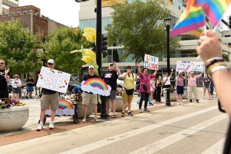 Evanston Pride Car Parade event with folks standing on the road cheering with Pride signs
