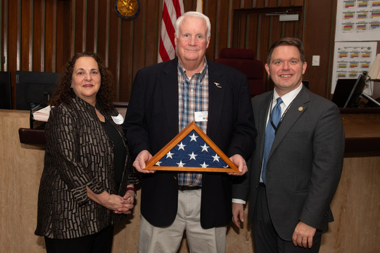 Man holding frame with American flag and woman to left, man to right 