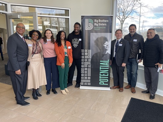 eight people standing next to a black and white sign 