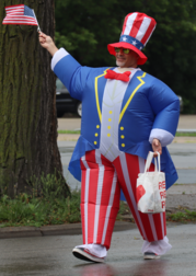 Man in Uncle Sam blow-up suit marches in the Oak Park Fourth of July Parade with an American flag