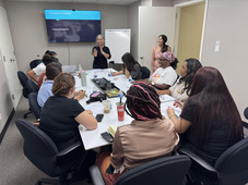 Participants sit around a table and listen to a person presenting