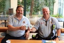 Lieutenant Steve Ausmann and Deputy Chief Robert Murphy of the Oak Park Fire Department smile and raise their cups while seated at a coffee shop