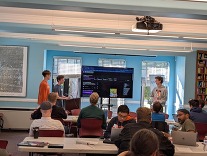 Participants stand in front of a screen and present their project at Day in Our Data