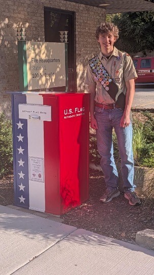 An Eagle Scout stands next to a retired US flag dropbox outside the main Oak Park fire station 