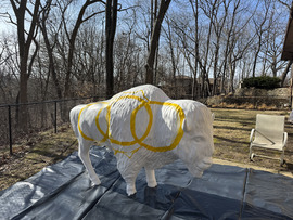 The bison sits outside, all-white with the exception of three gold circles, early in the painting process. 