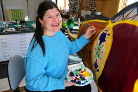 Artist Hattie Lee Mendoza smiles while painting details on the bison and holding a paint palette.