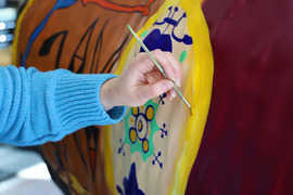 The artist's hand carefully applies brush strokes to gold circle on the bison.