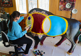 Artist Hattie Lee Mendoza paints details of the bison design with her back to the camera and a paint palette in her hand.