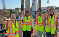 Garden club members holding up gardening tools in front of Municipal Building.