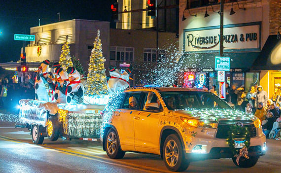 Christmas decorated cars and floats driving down main street at night.