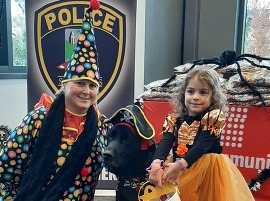 A little girl and a woman are dressed in costume and pose with a k-9 unit dog.