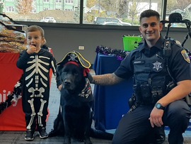Boy dressed as skeleton poses with k-9 unit dog dressed as a pirate and a police officer.