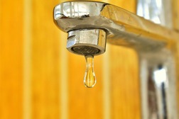 A faucet head with a single drip and a yellow background