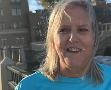 A woman stands next the Fox River with Hotel Baker in the background.
