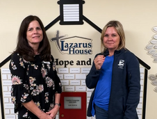 The Mayor on the right speaks with the executive director of Lazarus House in front of the donor wall at Lazarus House.