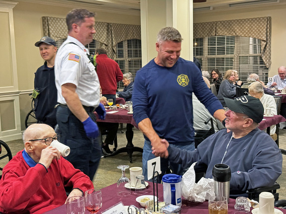 Firefighter shakes the hand of a resident of a senior living facility while talking and laughing.
