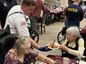 A firefighter serves a plate of pasta to residents in the dining room.